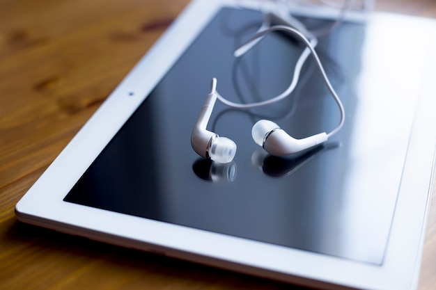 Foto um tablet branco e fones de ouvido brancos repousam sobre uma mesa de madeira