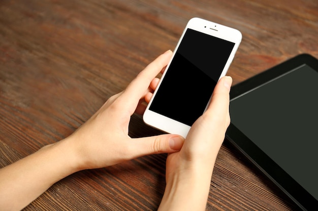 Um tablet e mãos femininas usando telefone celular no fundo de madeira