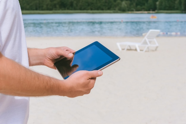 Um tablet nas mãos de um cara na praia.