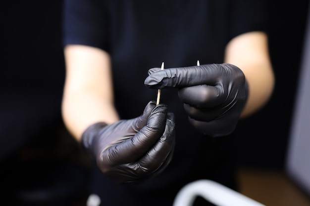 Um tatuador de luvas pretas segura um palito de dente à sua frente e o envolve com um pedaço de algodão