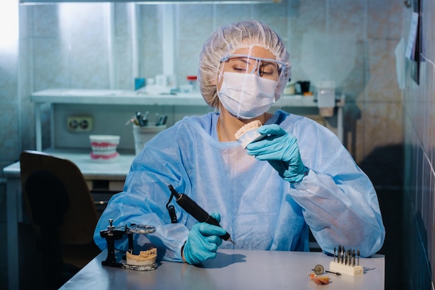 Um técnico dentário em roupas de proteção está trabalhando em um dente protético em seu laboratório