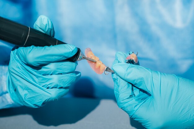 Um técnico dentário mascarado e com luvas trabalha em uma prótese dentária em seu laboratório.