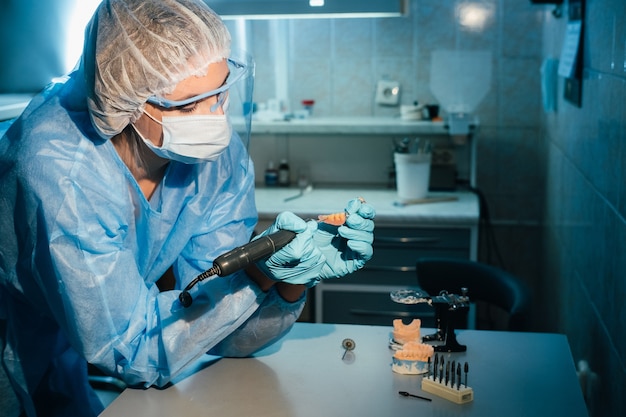 Um técnico dentário mascarado e com luvas trabalha em uma prótese dentária em seu laboratório.