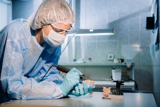 Um técnico dentário mascarado e com luvas trabalha em uma prótese dentária em seu laboratório.