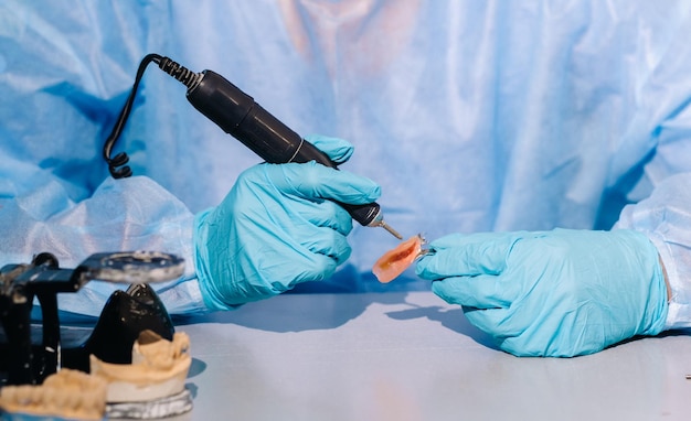 Um técnico dentário mascarado e com luvas trabalha em uma prótese dentária em seu laboratório.