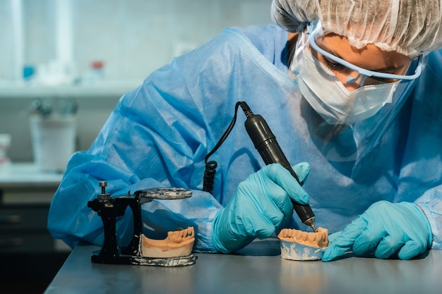 Um técnico dentário mascarado e com luvas trabalha em uma prótese dentária em seu laboratório.