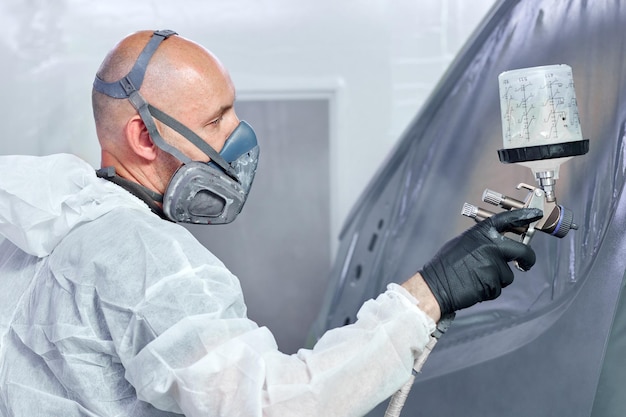 Um técnico garante um acabamento impecável usando um respirador enquanto pinta peças de carro em uma cabine de pintura profissional