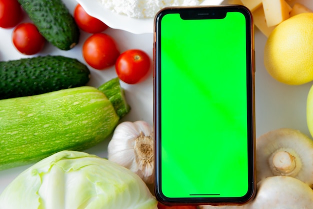 Um telefone com tela verde está entre frutas, verduras e laticínios foto de alta qualidade