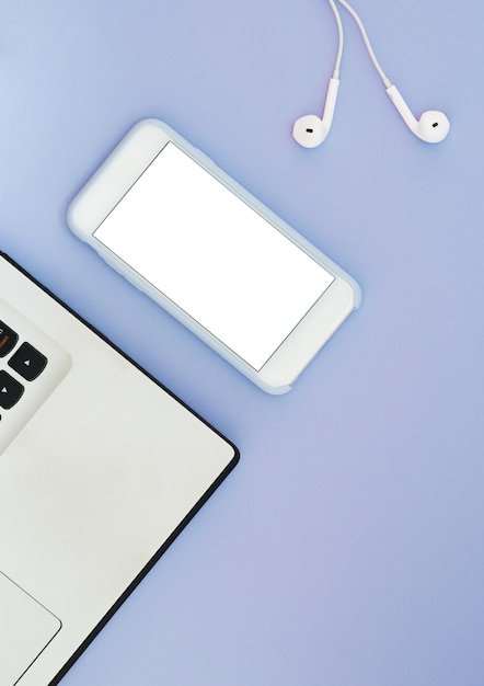 Um telefone com uma tela branca, um laptop e fones de ouvido em um fundo azul. gadgets lay plana e lugar para texto.