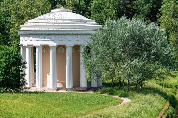 Um templo de estilo clássico em um belo parque de verão Campo verde com flores brancas e amarelas ao ar livre na natureza no verão. Campo de verão verde brilhante durante o dia