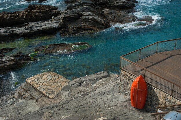 um terraço de praia feito de tábuas na costa com rochas do Mar Mediterrâneo um bote salva-vidas vermelho