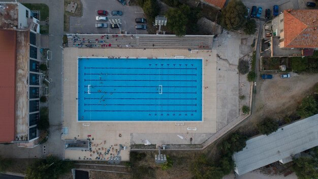 Um tiro de cima para baixo diretamente acima de uma piscina vazia cercada por grama verde e árvores em uma manhã nublada