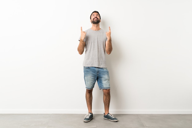 Um tiro de corpo inteiro de homem bonito com barba surpreso e apontando para cima