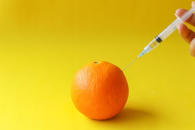 Um tiro de srynge para fruta laranja para fazê-la crescer em fundo amarelo o conceito de genética alimentar