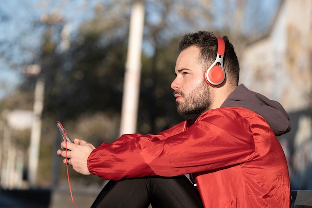 Um tiro do close up de um jovem macho no fone de ouvido vermelho, ouvindo música enquanto trabalhava na rua