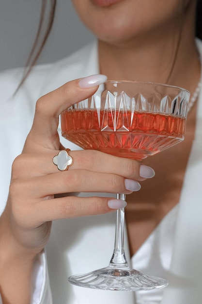 Um tiro vertical de uma mulher caucasiana segurando um copo de coquetel com um anel no dedo
