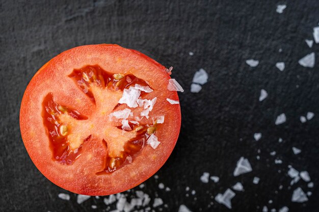 Um tomate partido ao meio polvilhado por flocos de sal na ardósia preta