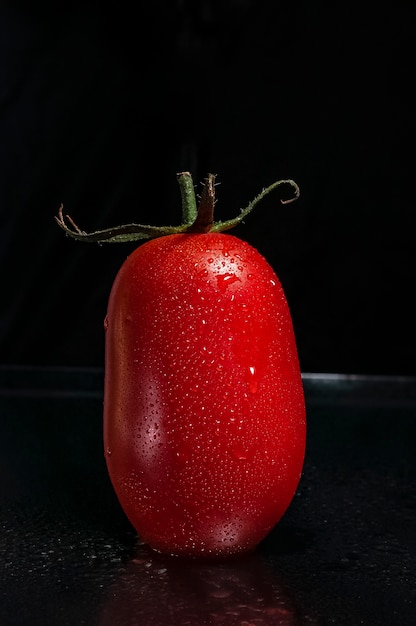 Um tomate vermelho, fresco, maduro e suculento com folhas verdes e gotas de água no escuro