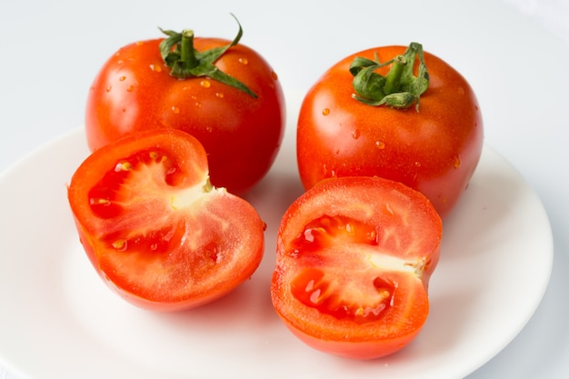 Um tomate vermelho maduro com gotas de água isoladas em um fundo branco.