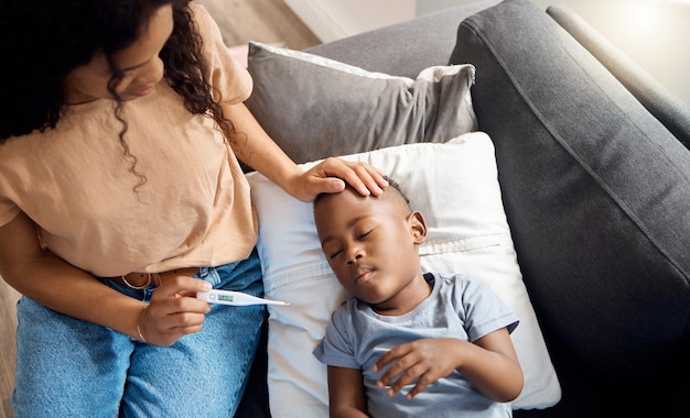 Um toque de mãe pode fazer você se sentir muito melhor. Tiro de alto ângulo de uma jovem mãe verificando a temperatura de seus filhos doentes em casa.