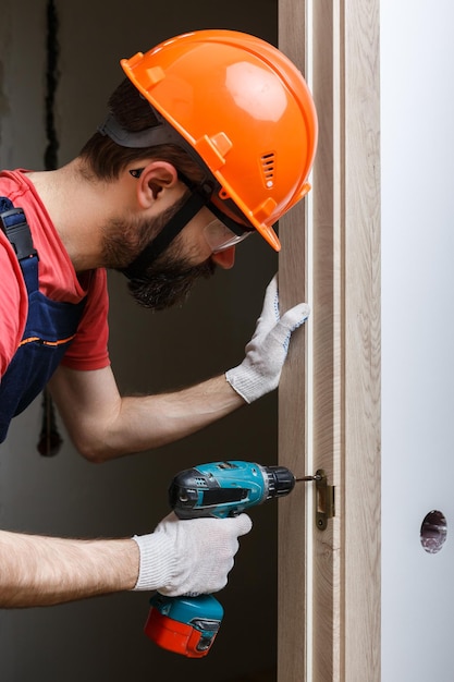 Um trabalhador com uma broca em um capacete laranja instala uma porta em casa