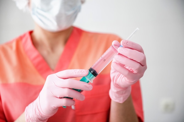 Um trabalhador da área médica com um manto rosa, boné branco e luvas cor de rosa segura uma seringa com uma vacina