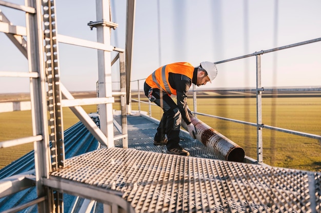 Um trabalhador da construção de metal está realocando um tubo enferrujado em pé na altura