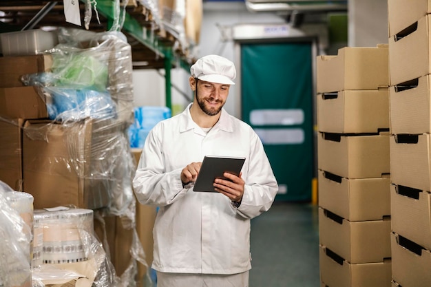 Um trabalhador da indústria de alimentos está usando tablet para inventariar no armazenamento e sorrindo para ele