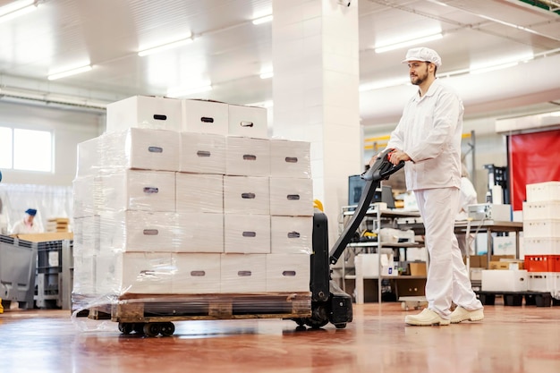 Um trabalhador de fábrica de carne empurrando empilhadeira e realocando carne fresca embalada