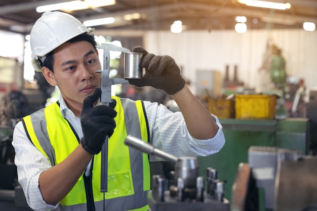 Um trabalhador de óculos em pé perto de um equipamento industrial e verifica a produção. homem operando máquina na fábrica