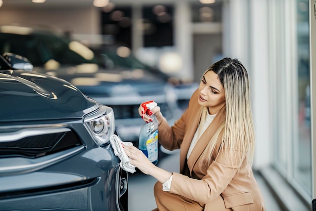 Um trabalhador de showroom de automóveis está agachado ao lado de um carro e limpando-o com detergente