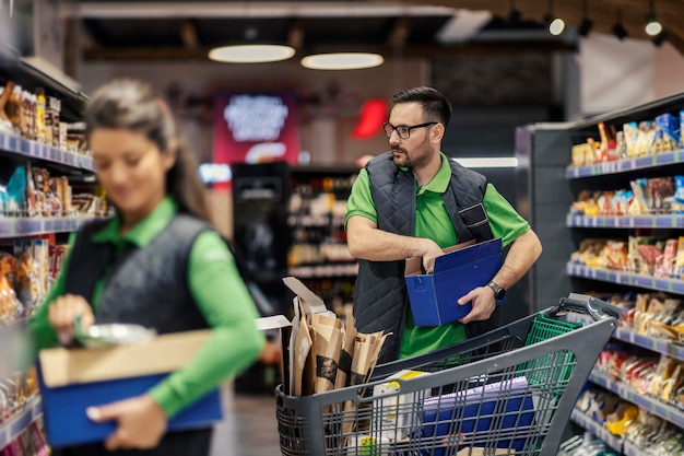 Um trabalhador de supermercado focado está organizando mantimentos nas prateleiras do mercado