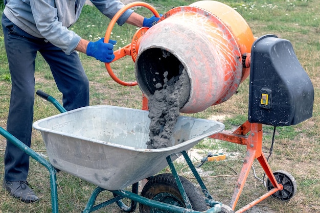 Foto um trabalhador derrama concreto de argamassa de cimento de um misturador de concreto em um carrinho de mão preparação de argamassa de cimento no canteiro de obras