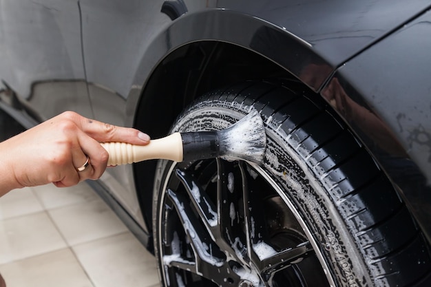 Foto um trabalhador do sexo masculino lava um carro preto com uma escova especial para rodas fundidas e esfrega a superfície para brilhar em uma oficina de detalhamento de veículos indústria de serviços automotivos