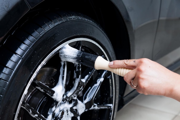 Foto um trabalhador do sexo masculino lava um carro preto com uma escova especial para rodas fundidas e esfrega a superfície