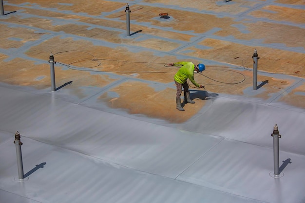 Um trabalhador do sexo masculino segurando uma pistola de pulverização industrial usada para a superfície do tanque da placa do telhado na pintura industrial de aço