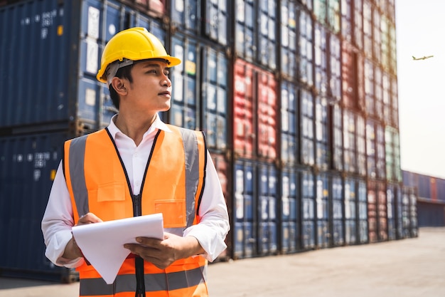 Foto um trabalhador em pé e usar um capacete amarelo controla o carregamento e verifica a qualidade dos contêineres do navio de carga para transporte, importação e exportação