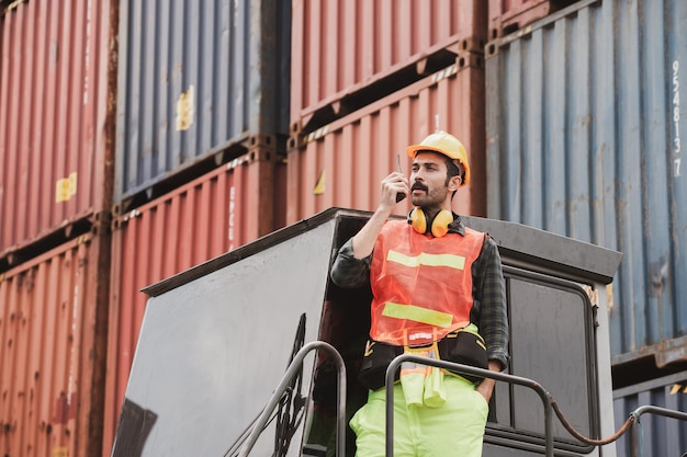 Foto um trabalhador em pé e usar um capacete amarelo controla o carregamento e verifica a qualidade dos contêineres do navio de carga para transporte, importação e exportação