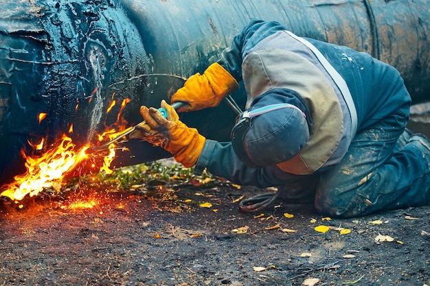 Um trabalhador em roupas de proteção corta um tubo de metal para gaseificação reparação e manutenção do gasoduto