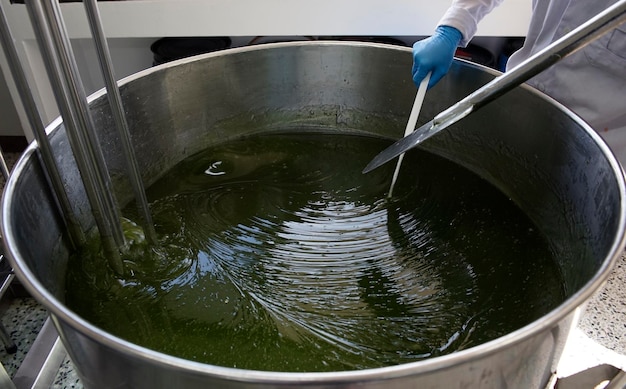 Um trabalhador está usando uma espátula de metal para misturar gel verde em um tanque homogeneizador