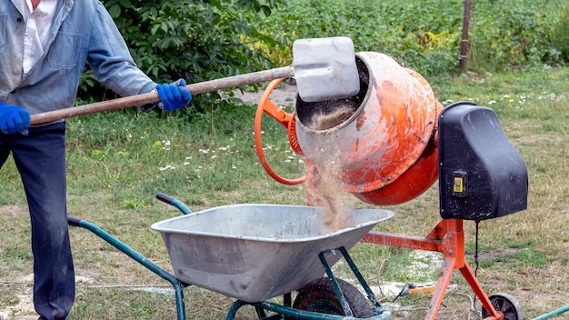 Um trabalhador joga areia em um misturador de concreto preparando argamassa de cimento