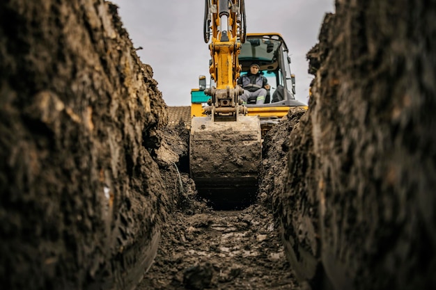 Um trabalhador na escavadeira está cavando a terra e fazendo a fundação no canteiro de obras