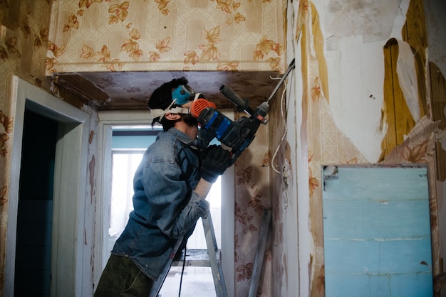 Um trabalhador perfura uma parede usando um perfurador. Reparo no apartamento