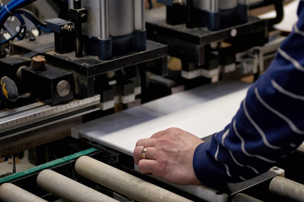 Um trabalhador processa espaços em branco de móveis em uma máquina-ferramenta em uma fábrica. Produção industrial de móveis.