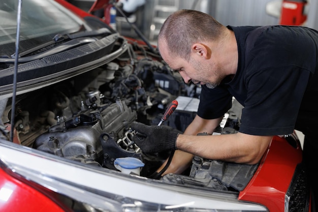 Um trabalhador um reparador reparando um carro O capô aberto do carro na garagem de reparação