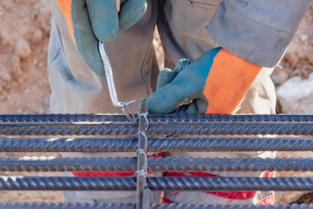 Um trabalhador usa arame de amarração de aço para prender hastes de aço a barras de reforço Closeup de estruturas de concreto armado de uma gaiola de reforço de metal