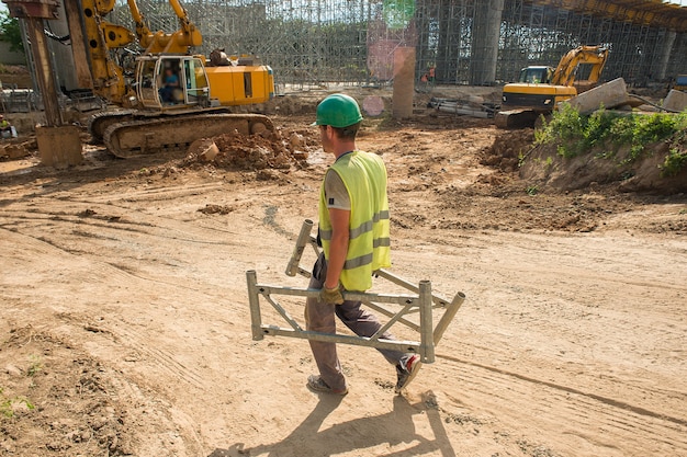 Um trabalhador usando um capacete de segurança carrega partes do andaime em um canteiro de obras
