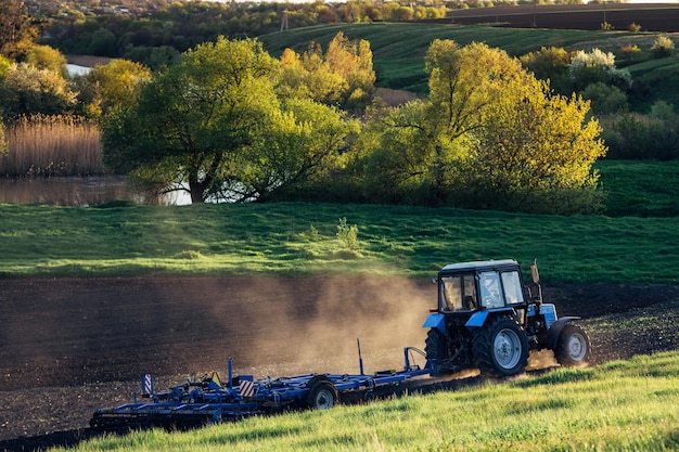 Um trator agrícola cultiva a terra no contexto de uma bela paisagem rural