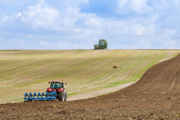 Um trator com um grande arado ara um campo. Trator com anexo agrícola. Preparação de terreno para semeadura.