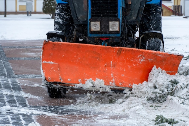 Um trator limpa a neve na cidade no inverno após uma queda de neve Limpando as ruas da cidade da neve Motorista de trator no trabalho na praça da cidade durante uma tempestade de neve